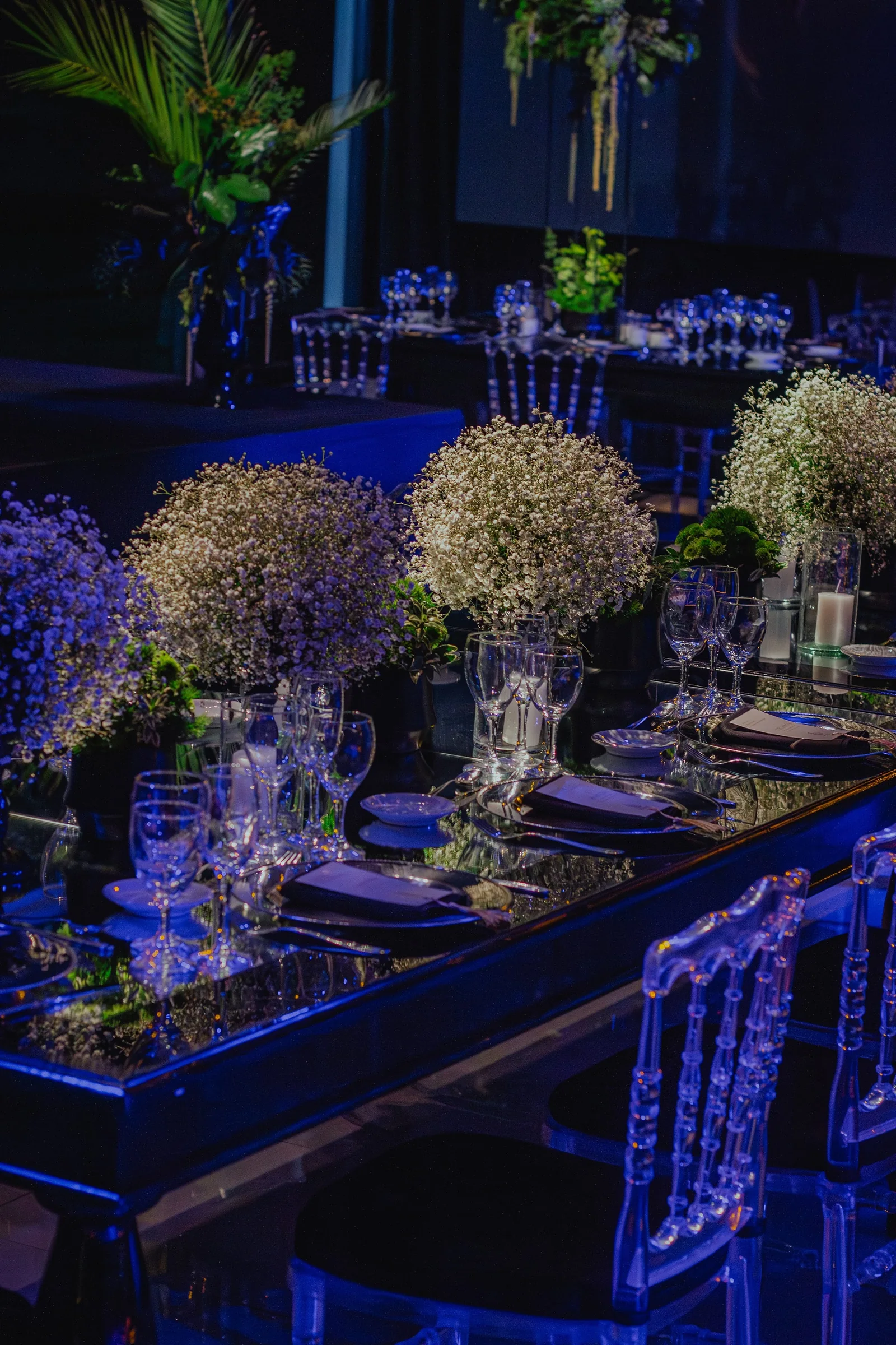 Salón de noche con mesas largas, nubes de gypsophila y luz azul